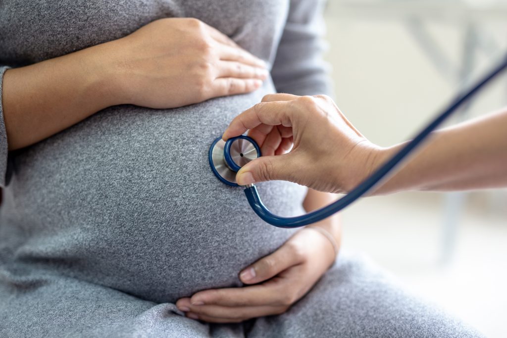A doctor with a stethoscope listening to a pregnant woman's uterus. C-section moms need the assistance of a confinement nanny for domestic tasks and recovery