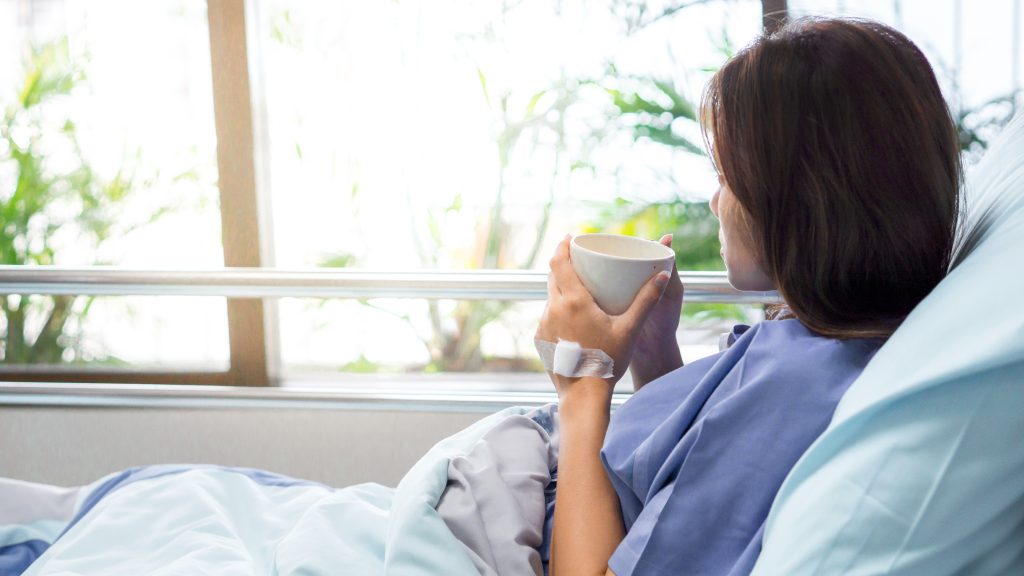 A recovering c-section mom drinking soup next to a window in her confinement bed. C-section moms need the assistance of a confinement nanny as they get home.
