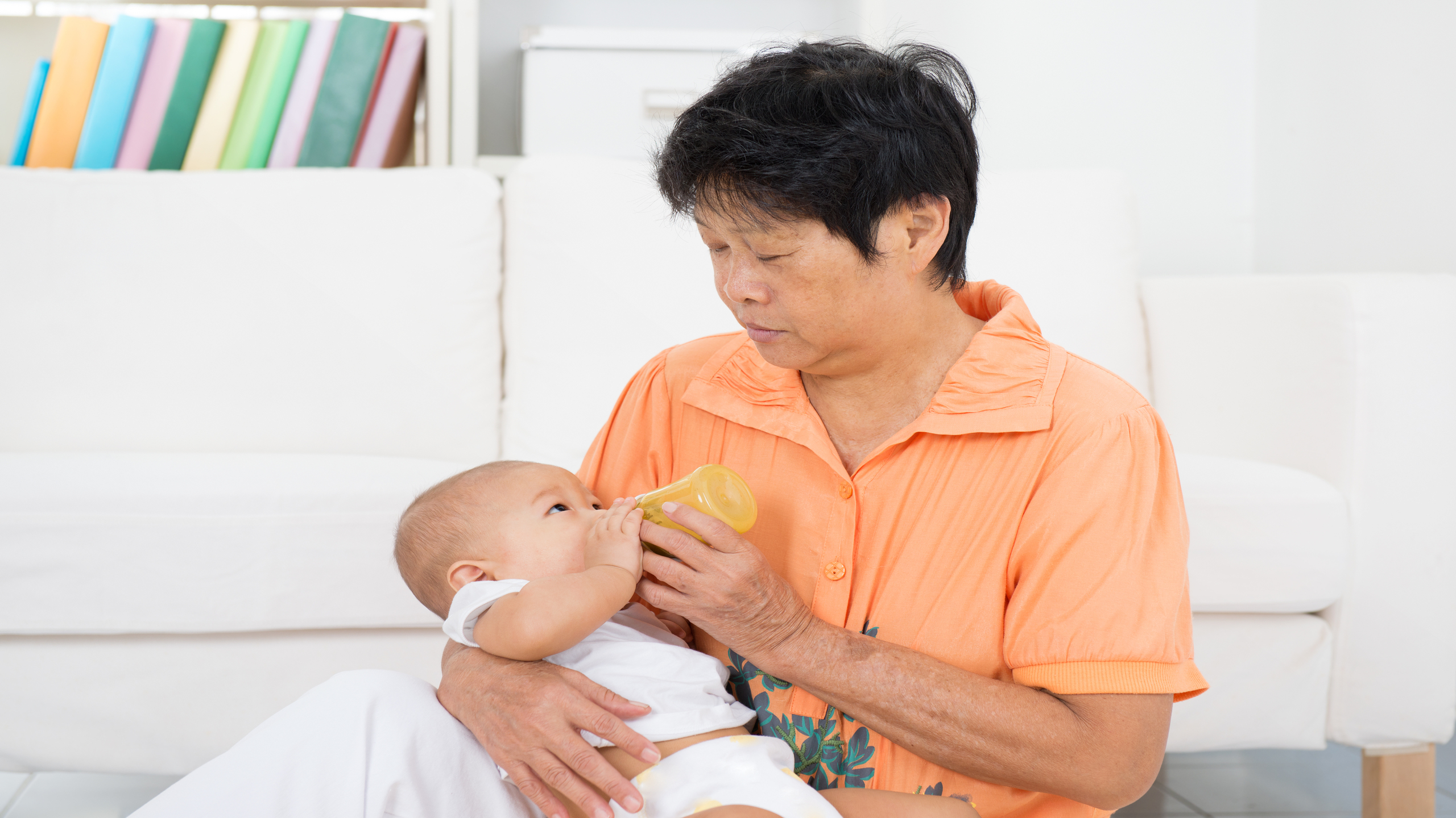 An elderly confinement nanny bottle-feeding a newborn