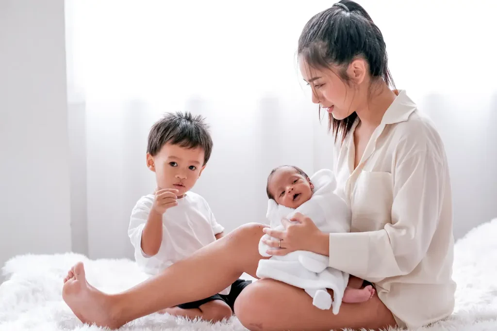 a mother holding her newly born second child, with her toddler sitting beside her - needing help of a confinement nanny in Singapore