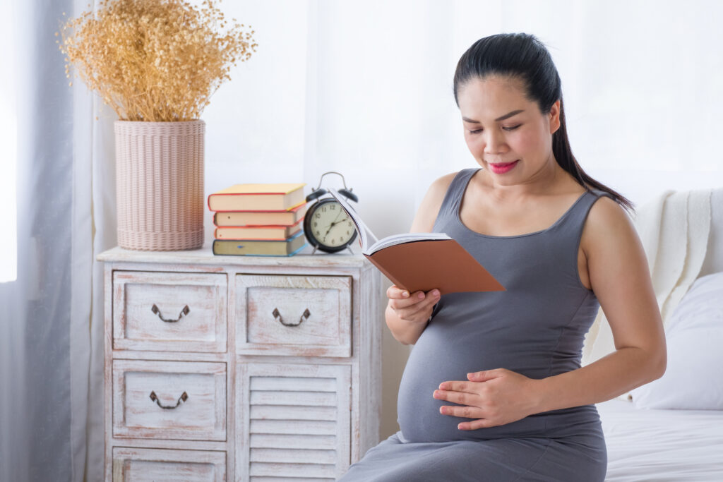 Pregnant woman reading a book while planning for her baby's arrival at home.