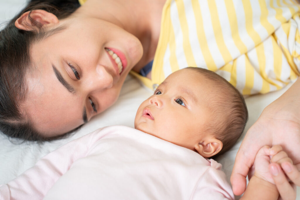 Mother smiling and holding her baby's hand during a bonding moment at home.