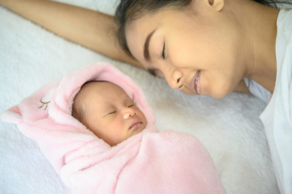 Mother watching over her sleeping newborn wrapped in a pink swaddle blanket.