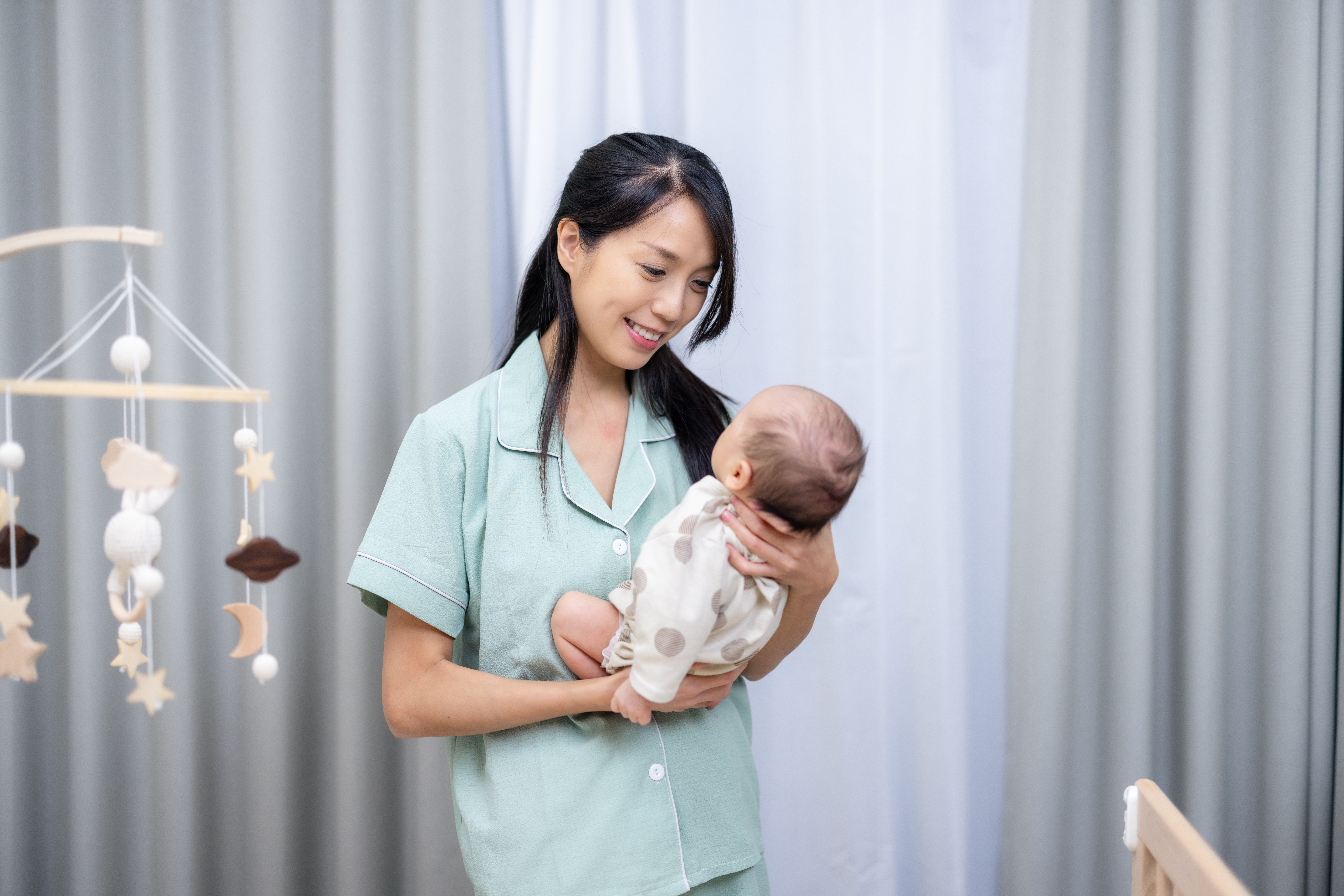 Confinement nanny carrying a newborn baby while providing postnatal care in a family home.